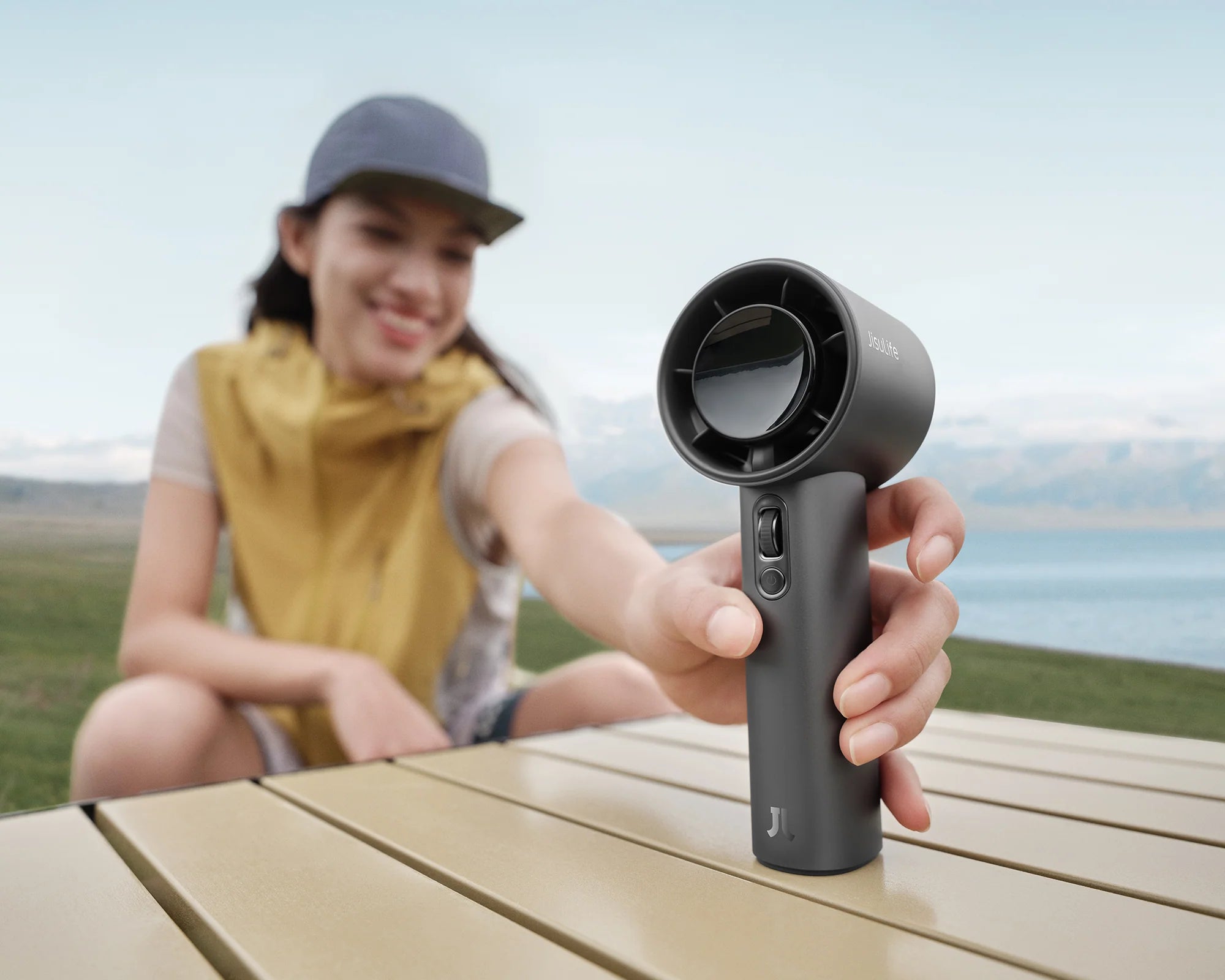 Woman places a portable handheld fan on a table during a lakeside break