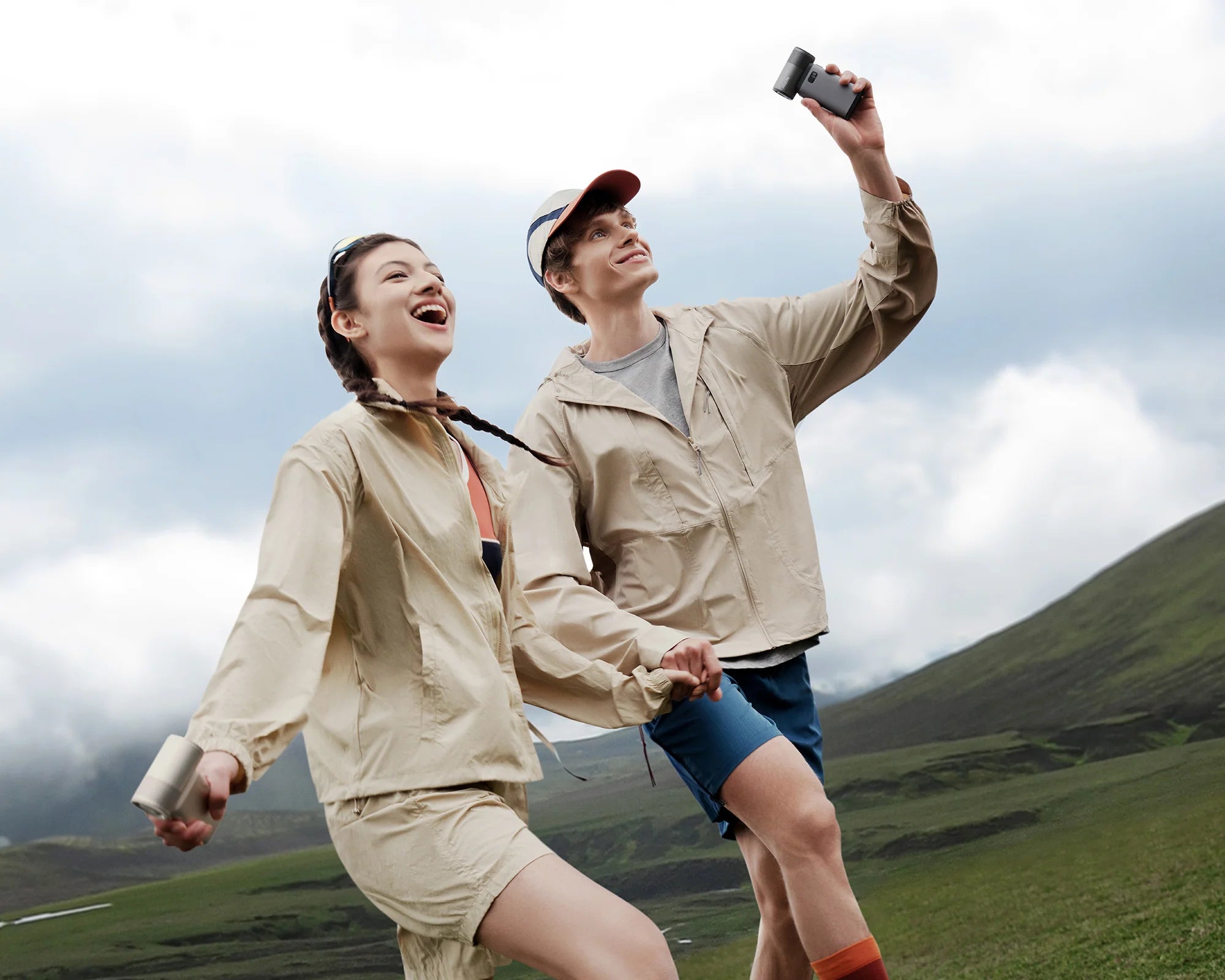 Two hikers use a portable rechargeable fan to stay cool on a mountain trail