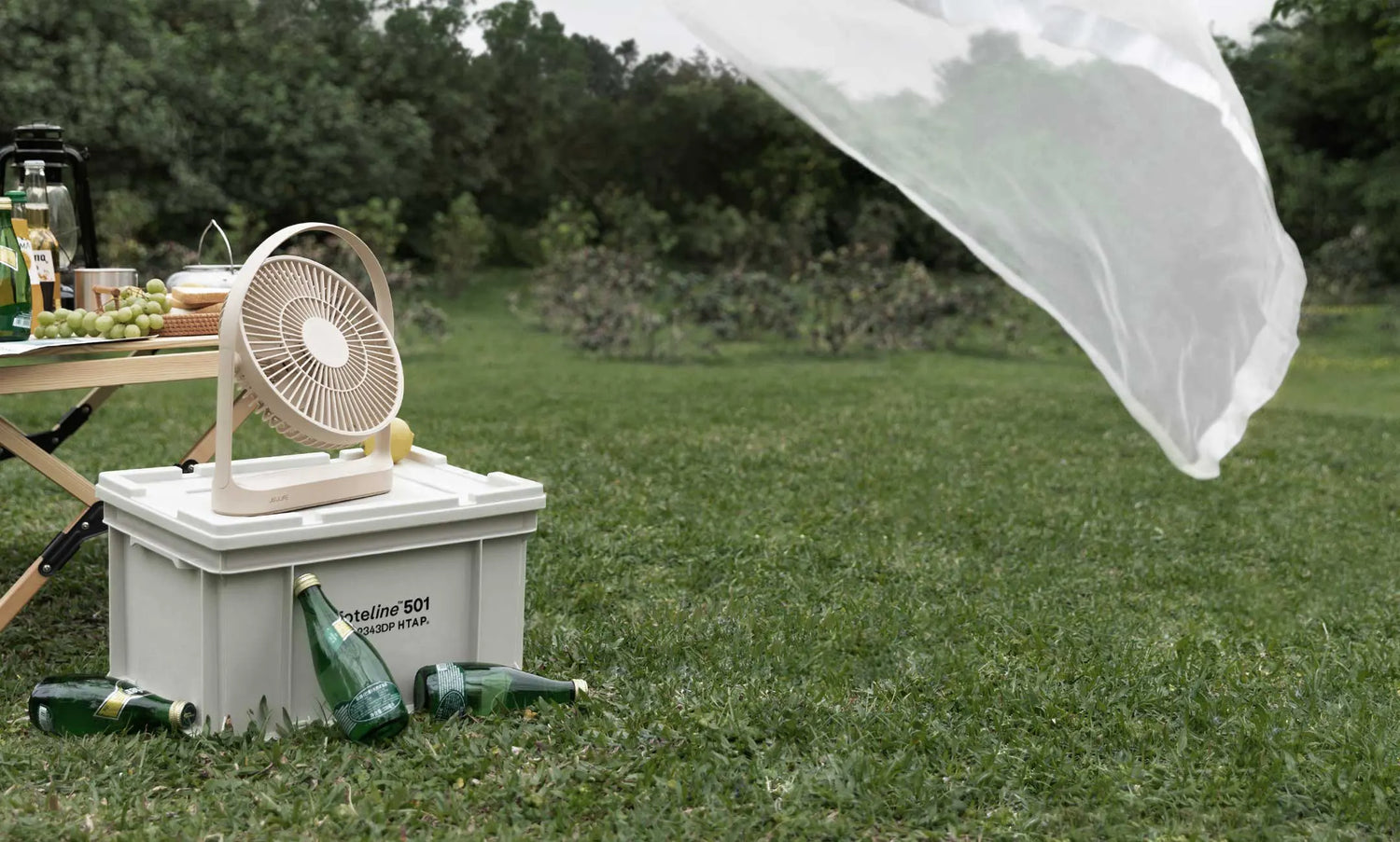 Portable fan resting on a white box during an outdoor picnic in a field.