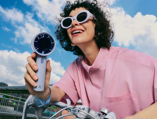 A stylish woman on a bike holds a portable handheld fan to stay cool in hot summer weather.