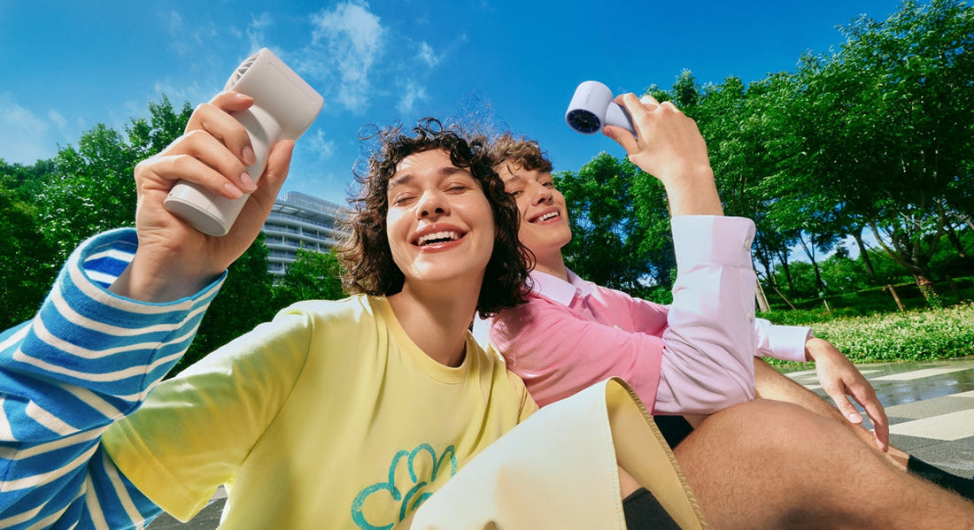 Happy couple enjoying the cool breeze from their portable grey and purple USB fans outdoors.