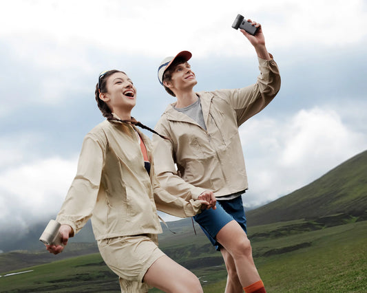 Two hikers use a portable rechargeable fan to stay cool on a mountain trail