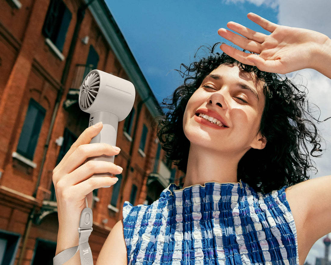 Woman holds a rechargeable portable fan in bright summer sun on a city street