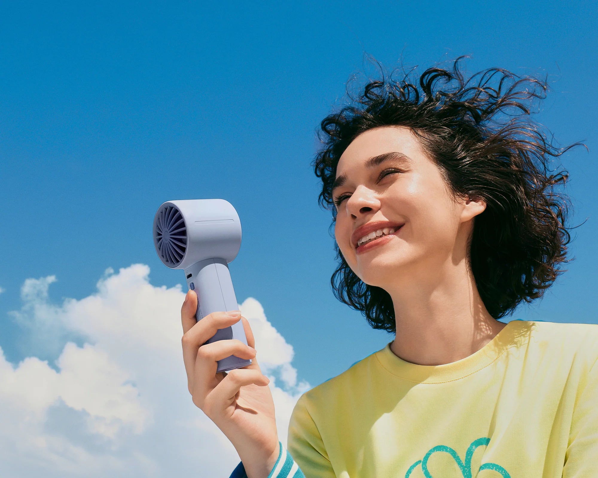 Woman holds a JISULIFE LIFE10S handheld fan under a bright blue sky