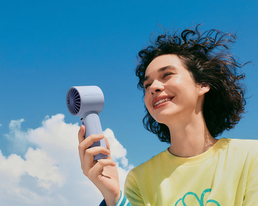Woman holds a JISULIFE LIFE10S handheld fan under a bright blue sky